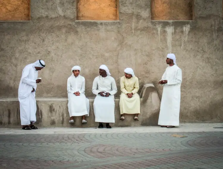 Arab men wearing traditional Arabic clothes sat on a wall in Bur Dubai